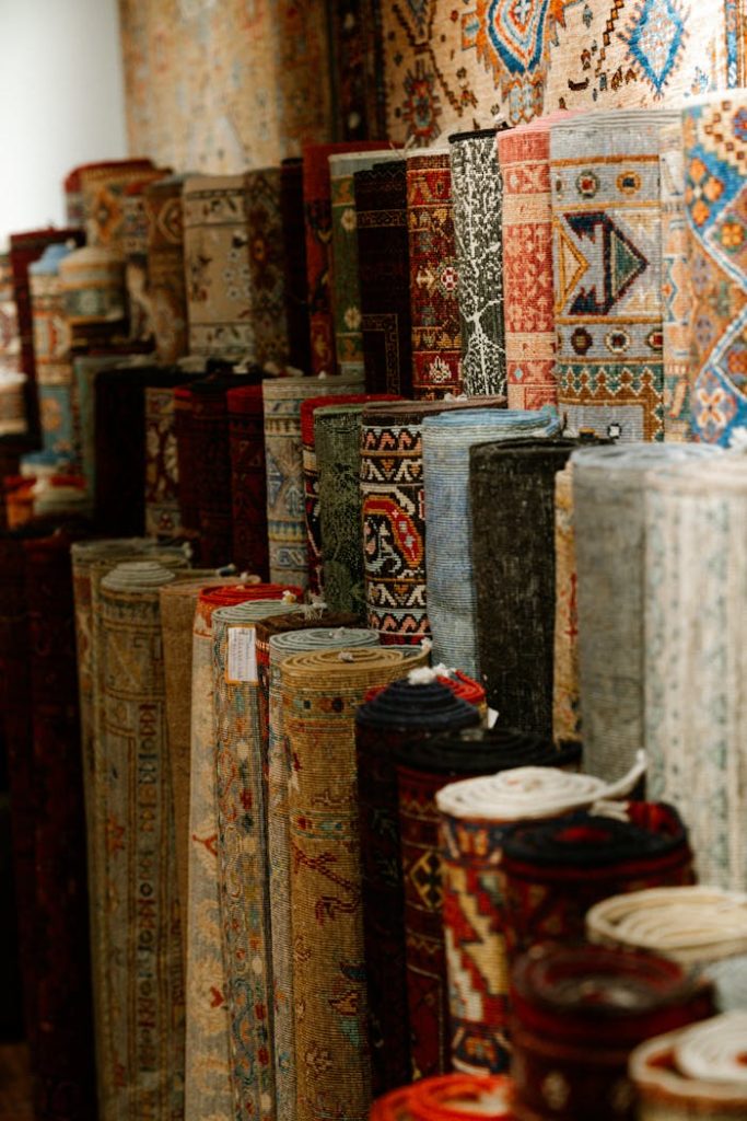 A colorful assortment of intricate Persian carpets rolled and displayed indoors, showcasing rich patterns and textures.