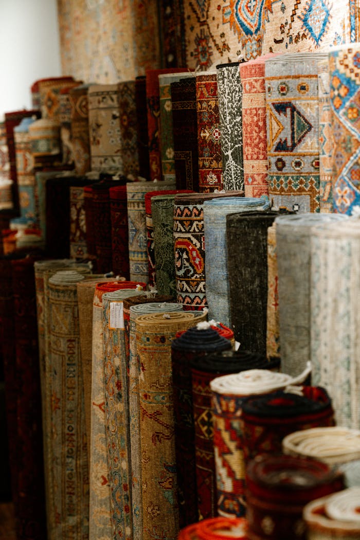 A colorful assortment of intricate Persian carpets rolled and displayed indoors, showcasing rich patterns and textures.