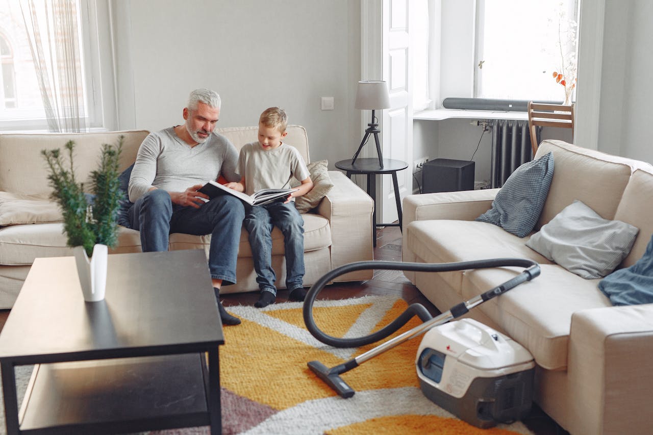 A grandfather and grandson enjoy reading together on a sofa in a cozy living room filled with natural light.