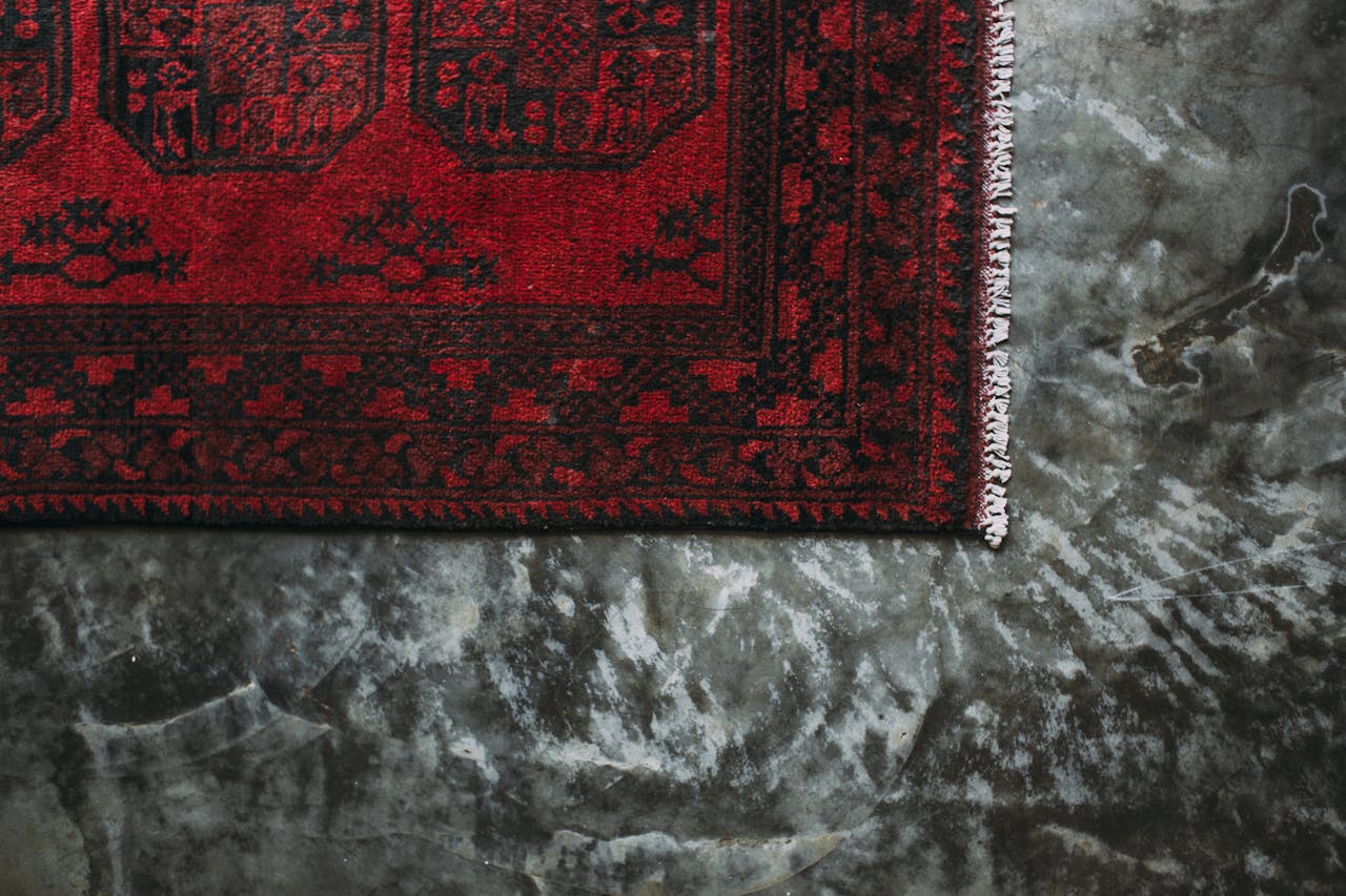 Close-up of a red floral patterned carpet on a textured concrete floor.