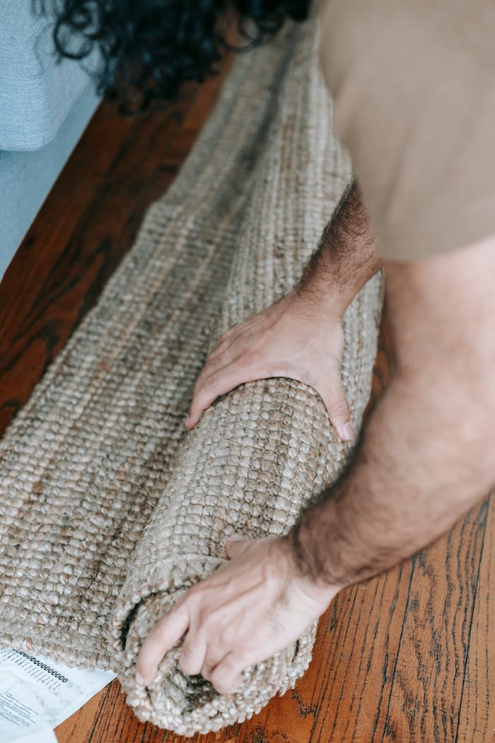 Close-up of a man rolling a carpet on wooden floor, suggesting moving or redecorating an apartment.
