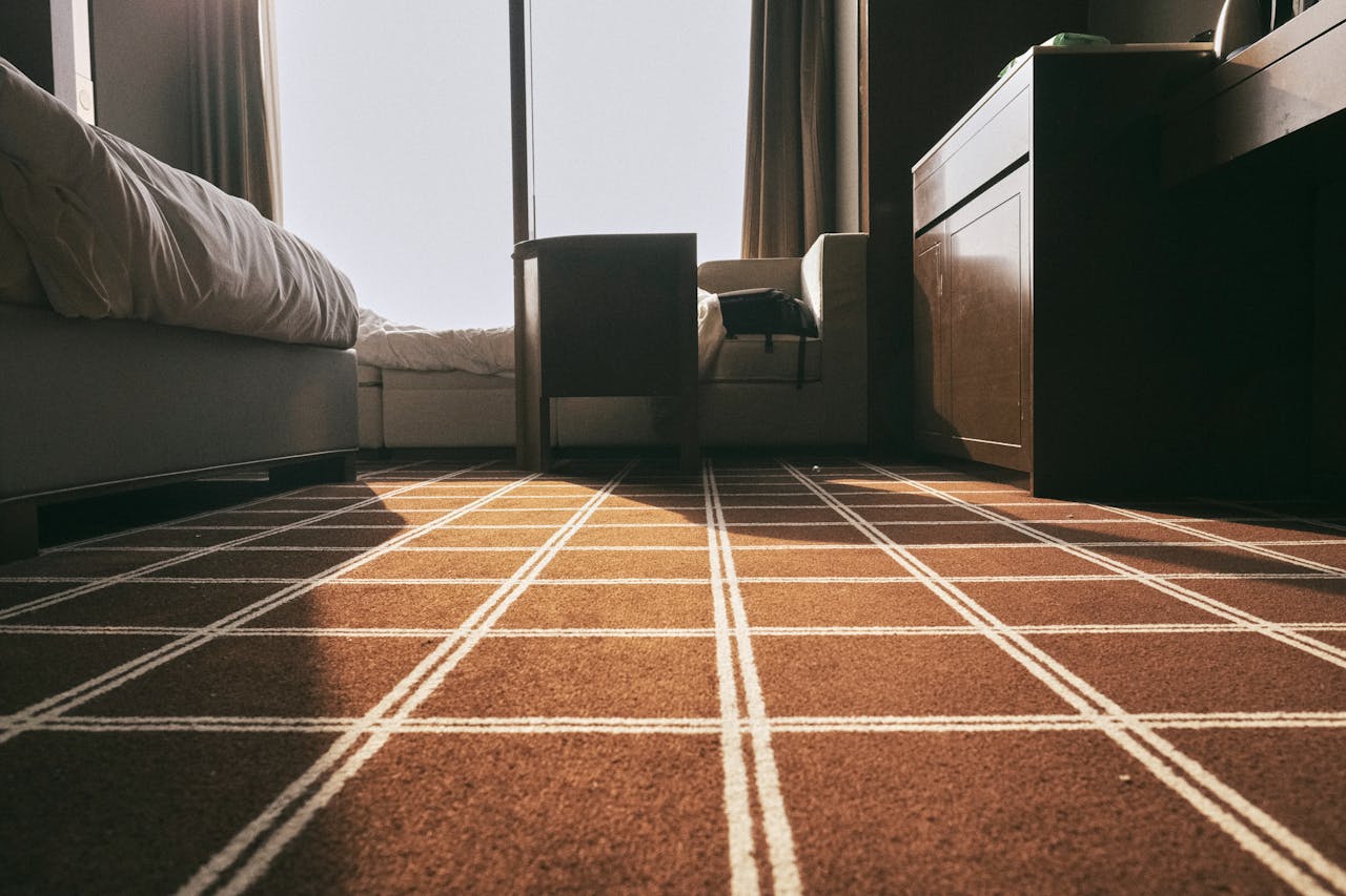 Low-angle view of a sunlit bedroom with patterned carpet and modern furniture, creating a warm atmosphere.